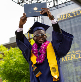 uc merced graduate hoisting up his diploma at commencement