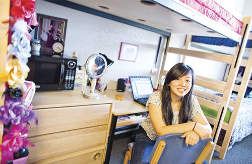A picture of a student sitting at her desk in her dorm space  