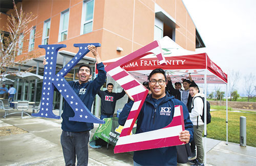 A picture of students holding a Fraternity logo outside their stand