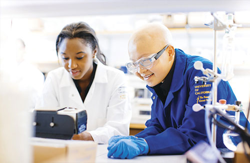 Two students collaborating in a lab wearing protective gear. 